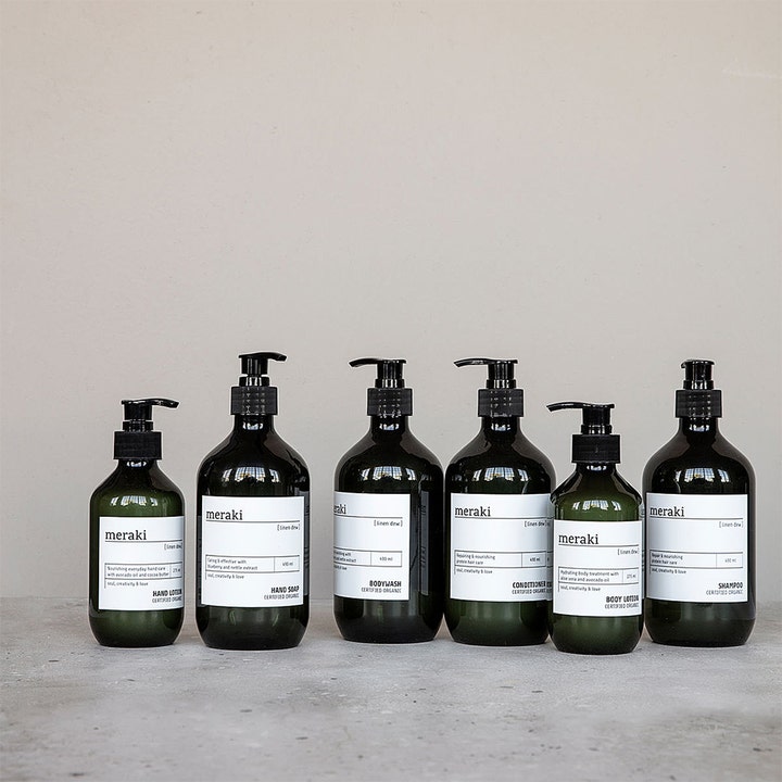 Meraki Linen Dew Hand Lotion 275 ml fugtgivende håndcreme i mørk flaske med pumpe i en stilren gruppeopstilling.
