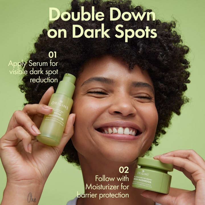 Origins Dr. Weil Mega-Mushroom 50 ml ansigtscreme til barrierebeskyttelse i grøn krukke holdt af smilende kvinde.