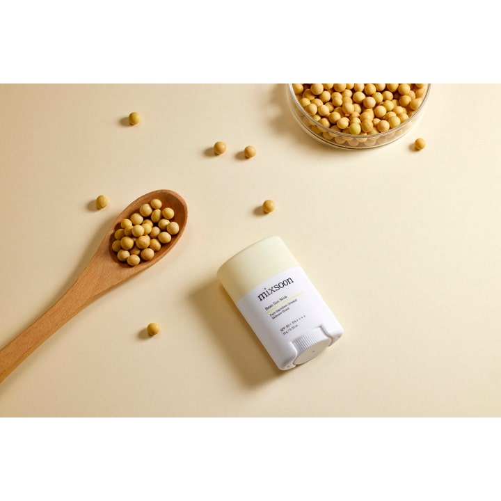 Mixsoon Bean Sun Stick 15 g solstift med SPF 50+ vist sammen med sojabønner på en træske og beige baggrund