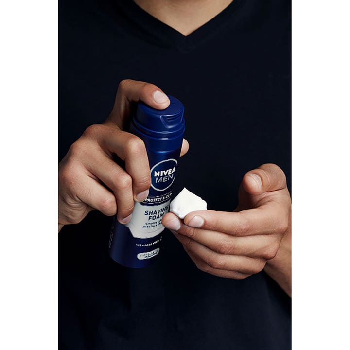 NIVEA Protect & Care Shaving Foam 200 ml i blå spraydåse med hvidt barberskum på en mands fingerspids