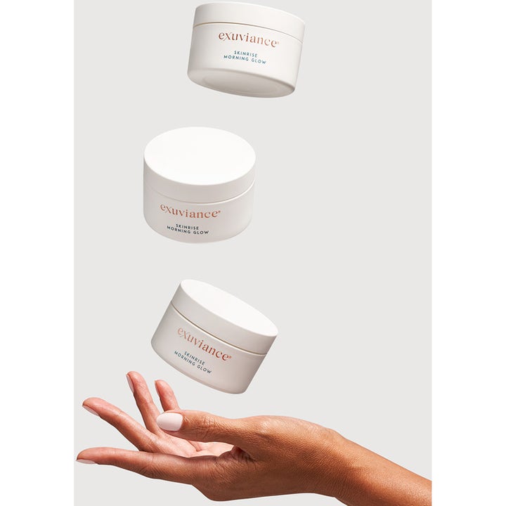 Exuviance SkinRise Morning Glow 36 stk glødgivende serum i hvide krukker svævende over en åben hånd
