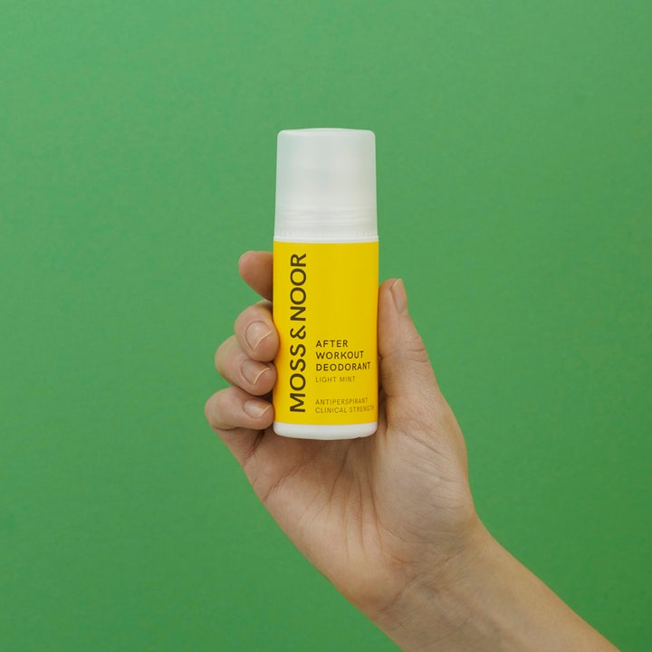 Moss & Noor After Workout Deodorant Light Mint 60 ml antiperspirant i gul flaske holdt i en hånd mod grøn baggrund