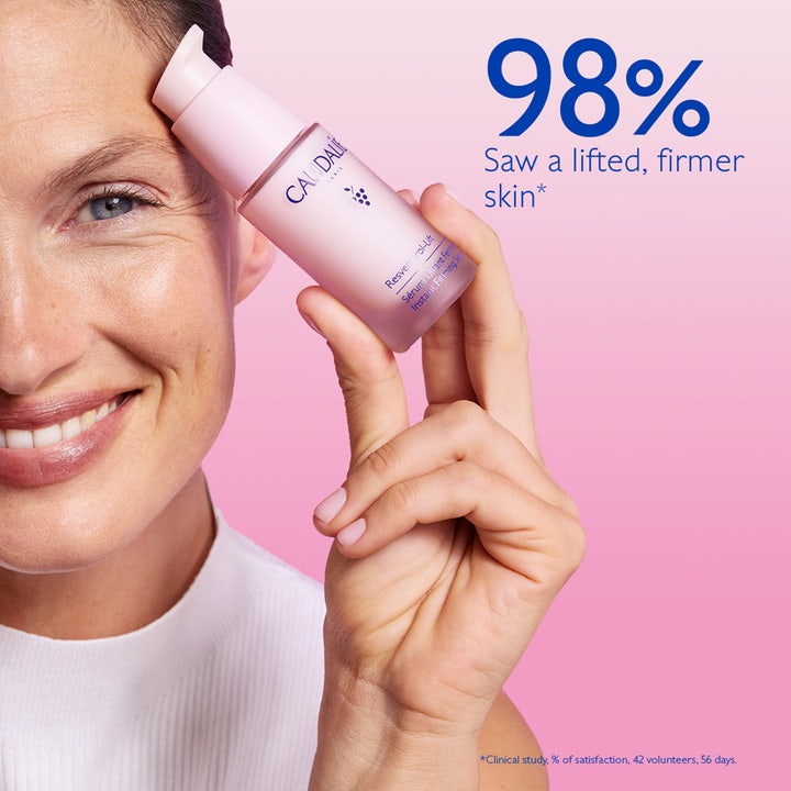 Caudalie Resveratrol-Lift Instant Firming Serum 30 ml i lyserød glasflaske holdt af en smilende kvinde