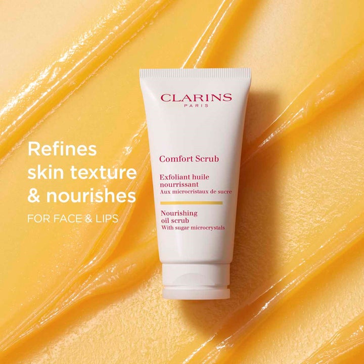 Clarins Comfort Scrub 50 ml nærende ansigtsskrubb giver blød hud vist mod en gul olietekstur med sukkerkrystaller
