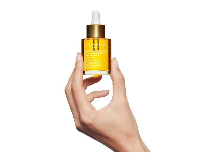 Clarins Blue Orchid Face Treatment Oil 30 ml fugtgivende ansigtsolie i glasflaske med guldlåg holdt i en hånd.