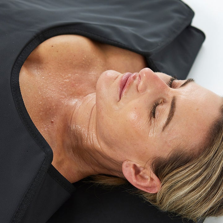 HigherDOSE Infrared Sauna Blanket infrarødt saunatæppe til restitution viser en svedende kvinde i det sorte tæppe.