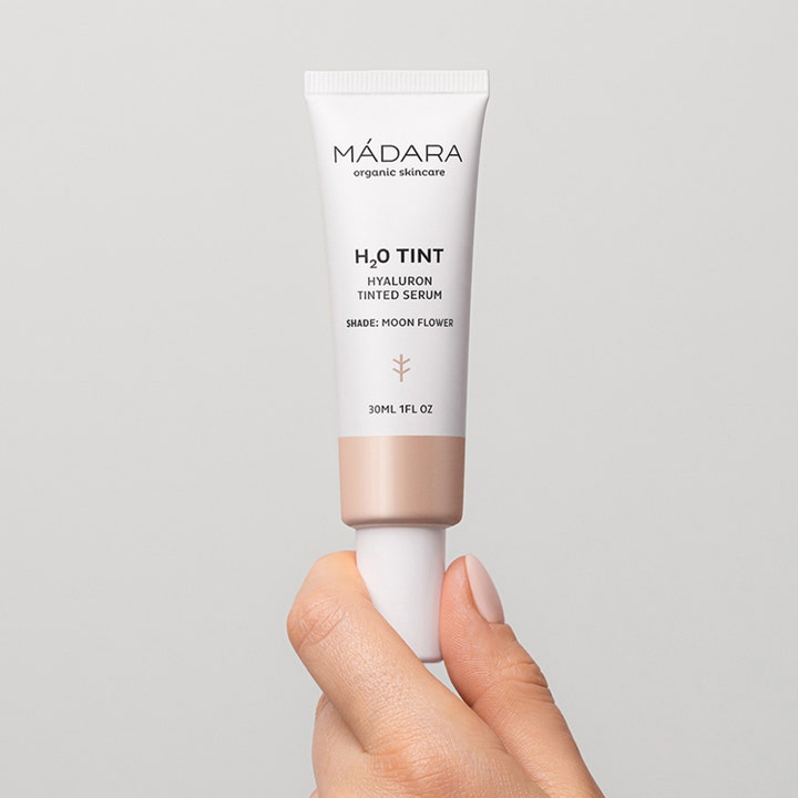 MÁDARA H2O Tint Hyaluron Tinted Serum 30 ml Moon Flower fugtgivende serum i hvid tube holdt af en hånd