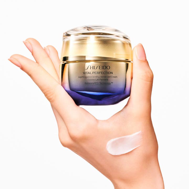 Shiseido Vital Perfection Advanced Day Cream 50 ml opstrammende dagcreme i guld og lilla krukke med swatch på en hånd