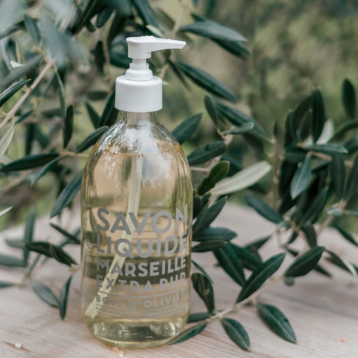 Compagnie de Provence Liquid Marseille Soap Olive Wood 495 ml håndsæbe i glasflaske omgivet af olivengrene