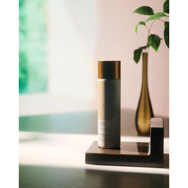 Sensai Silky Bronze Cooling Protective Suncare Spray 150 ml solspray SPF50 på en mørk stenplade ved en guldvase