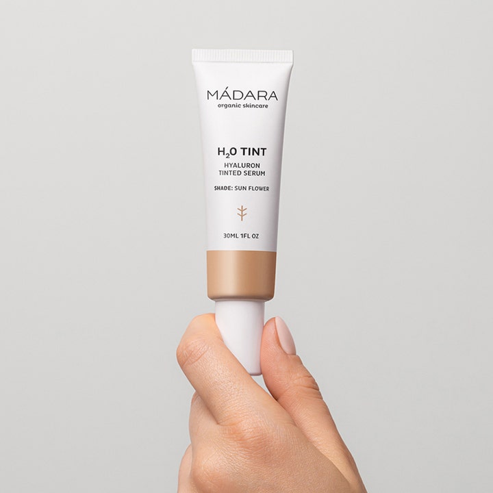 MÁDARA H2O Tint Hyaluron Tinted Serum 30 ml fugtgivende serum der giver glød i hvid tube holdt af en hånd