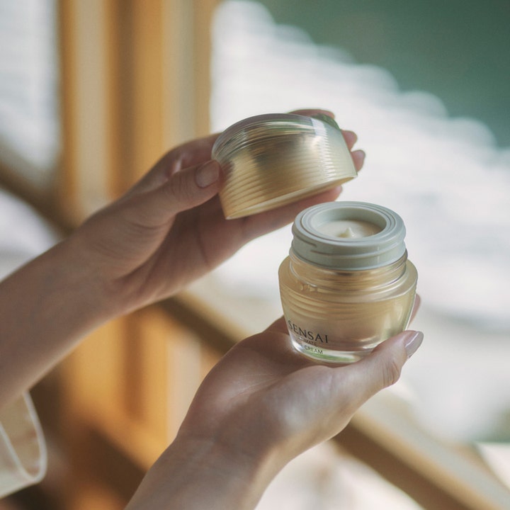 Sensai Ultimate The Cream 40 ml fugtgivende ansigtscreme i en luksuriøs guldfarvet glaskrukke i hænderne.