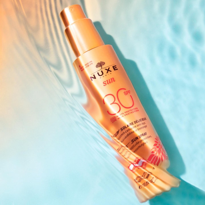 Nuxe Sun Spray SPF30 184 g solcreme i orange sprayflaske der flyder i blåt vand med sollys