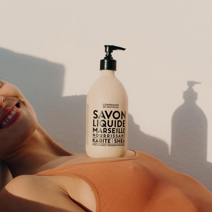 Compagnie de Provence Liquid Marseille Soap Shea 495 ml nærende håndsæbe i beige flaske placeret i varmt sollys