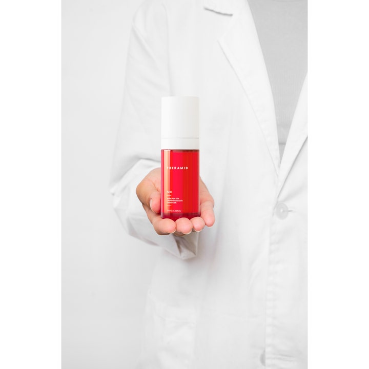 Niche Beauty Lab Theramid Azid 30 ml serum mod rødme i rød flaske som holdes af en person i hvid kitel.