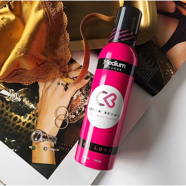 Cocoa Brown 1 Hour Tan Medium 150 ml selvbruner mousse i pink flaske vist i et livsstilsmiljø med luksuriøst tilbehør.