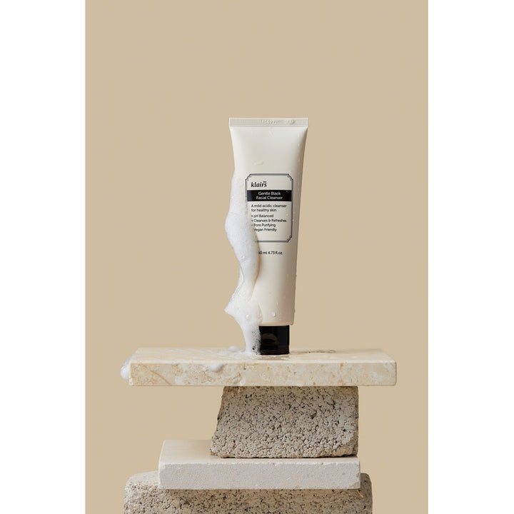 Klairs Gentle Black Facial Cleanser 140 ml mild ansigtsrens i tube omgivet af hvidt skum på en stenopsats