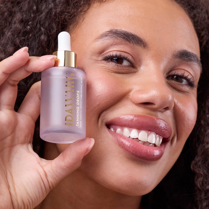 IDA WARG Beauty Tanning Drops 45 ml vegansk selvbruner i frosted flaske med guldhætte holdt af smilende kvinde