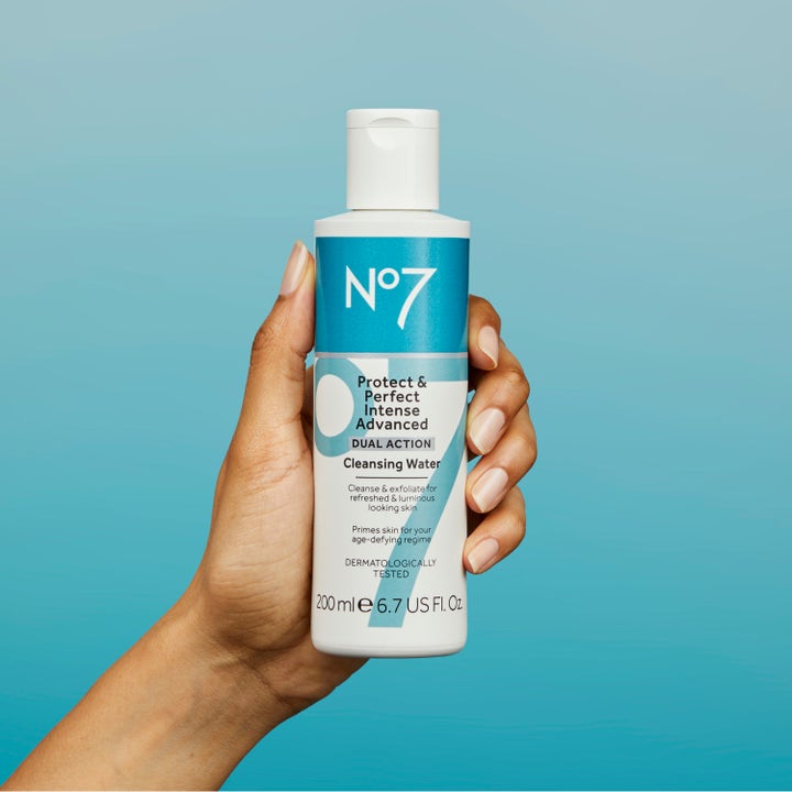 No7 Protect & Perfect Intense Advanced Cleansing Water 200 ml eksfolierende ansigtsrens i hånd mod blå baggrund