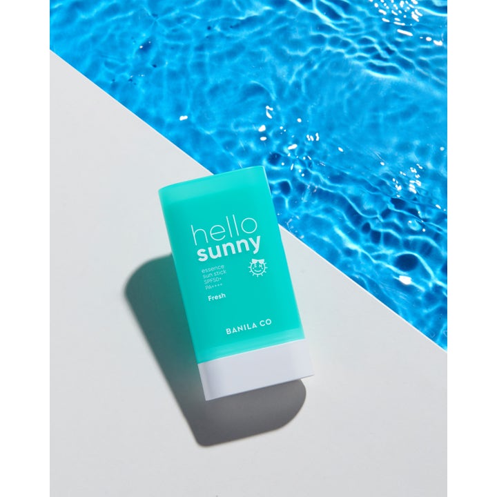 Banila Co Hello Sunny Essence Sun Stick 18,5 g SPF50+ Fresh solcreme i turkis hylster ved blåt poolvand.