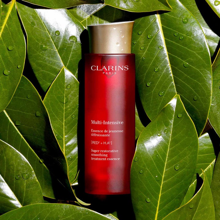 Clarins Super Restorative Treatment Essence 200 ml i rød flaske omgivet af grønne blade