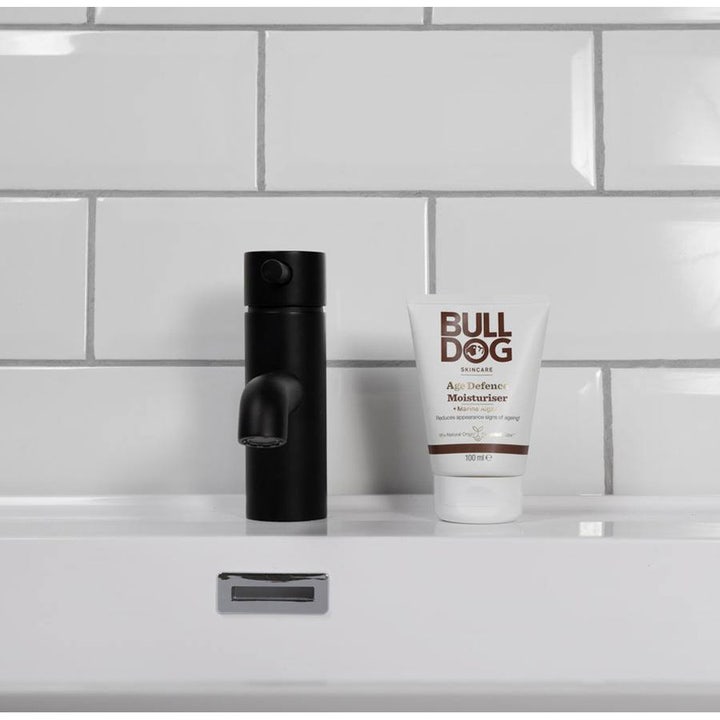 Bulldog Age Defence Moisturiser 100 ml fugtgivende ansigtscreme i hvid tube stående på en vask ved en sort vandhane