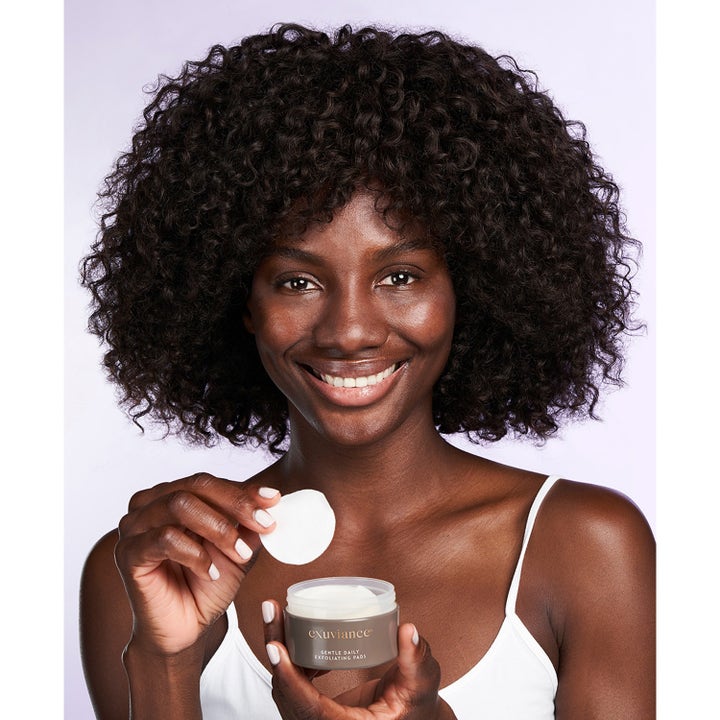 Exuviance Gentle Daily Exfoliating 60 Pads 55 ml giver glød vist med smilende kvinde der holder en hvid pad