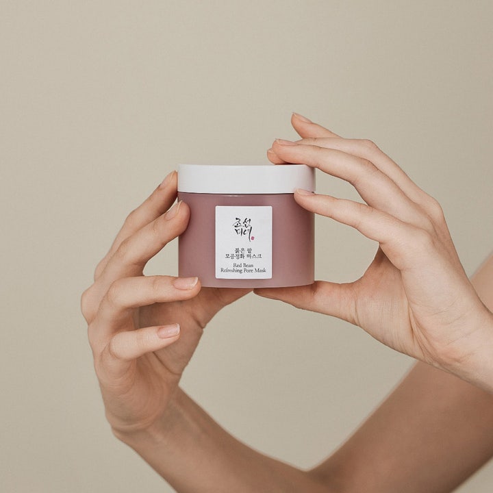 Beauty of Joseon Red Bean Refreshing Pore Mask 140 ml ansigtsmaske til hudpleje i mat rosa krukke holdt af to hænder.