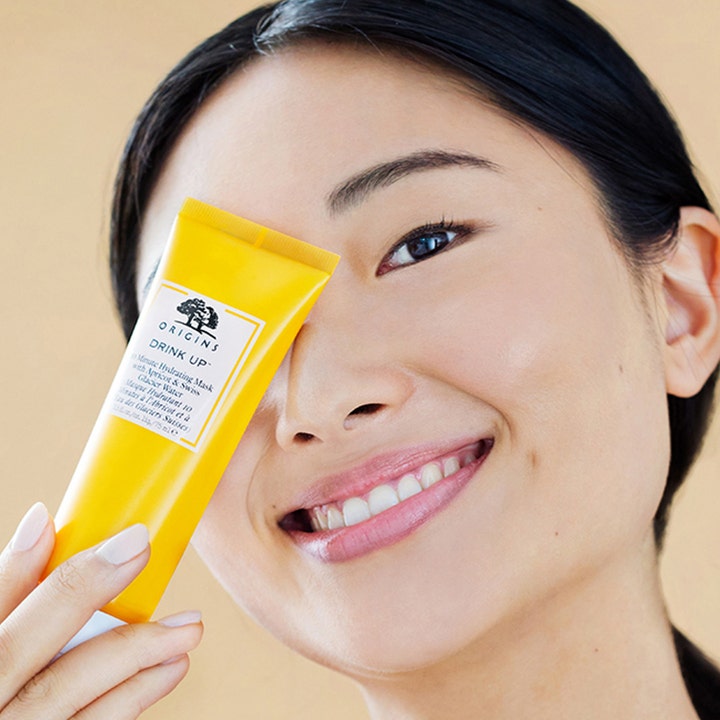 Origins Drink Up 10 Minute Mask 75 ml fugtgivende ansigtsmaske i gul tube vist med en smilende kvinde