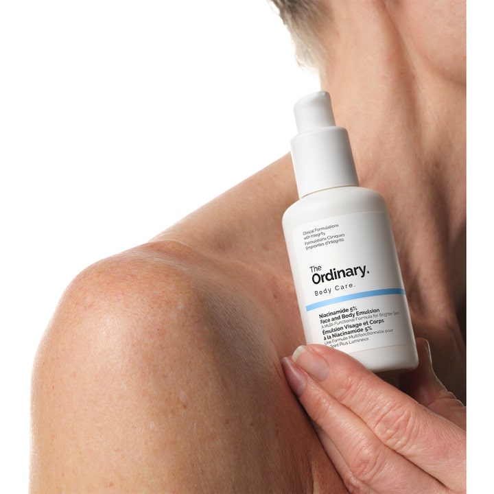 The Ordinary Niacinamide 5% Face & Body Emulsion 100 ml i hvid pumpeflaske vist mod bar hud på en skulder.