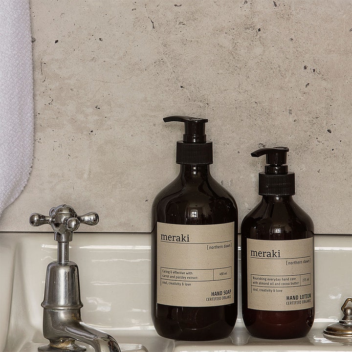 Meraki Northern Dawn Hand Soap 490 ml plejende håndtvæbe i mørk pumpeflaske på en hvid vask ved en stenvæg