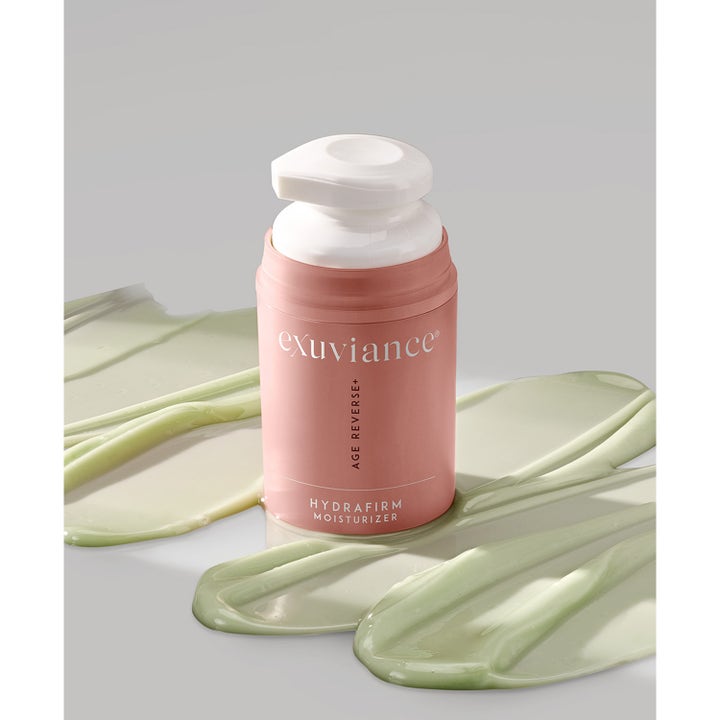 Exuviance Age Reverse Hydrafirm 50 g fugtgivende natcreme i pink pumpeflaske omgivet af grøn tekstur