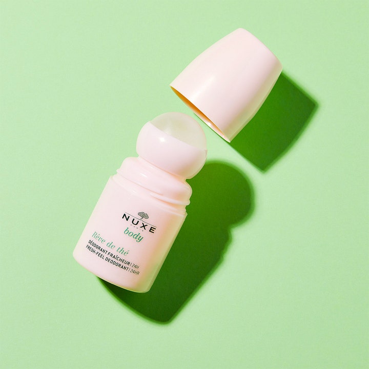 Nuxe Body Rêve de Thé 50 ml roll-on deodorant i lyserød emballage med låget taget af på grøn baggrund.