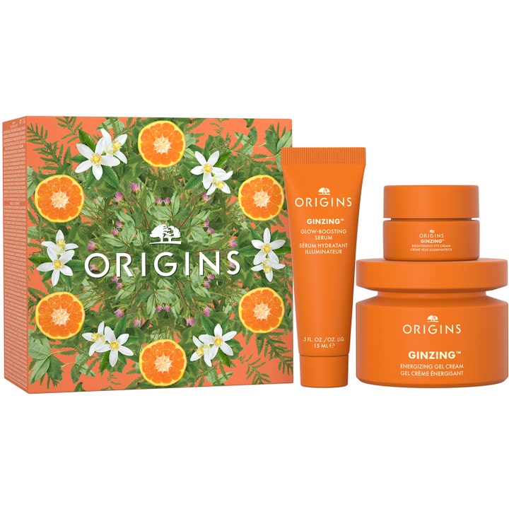 Origins GinZing hudplejesæt med serum, øjencreme og ansigtscreme i orange krukker ved siden af en blomstret æske.