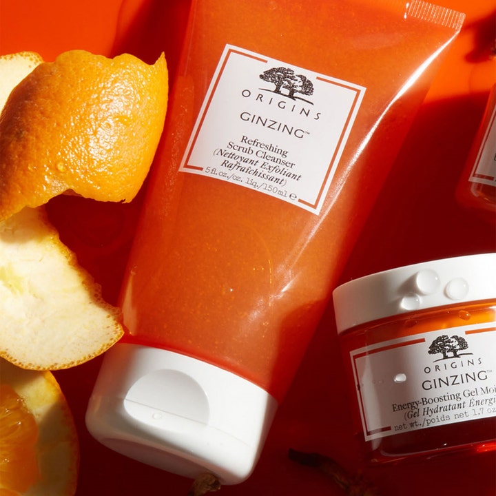 Origins GinZing Refreshing Scrub Cleanser 150 ml ansigtsskrubb i orange tube ved siden af friske appelsinskaller
