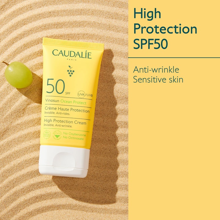 Caudalie Vinosun Protect Cream SPF50+ 50 ml rynkehæmmende solcreme i gul tube på sand med en grøn drue