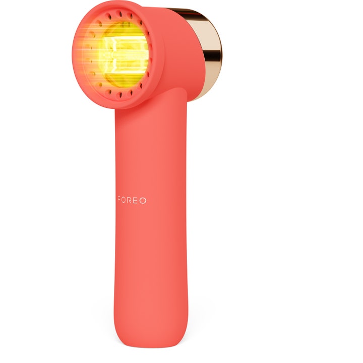 FOREO UFO 3 ansigtsbehandling med LED-lys i et koralrødt apparat med guld bagside der giver sund glød.