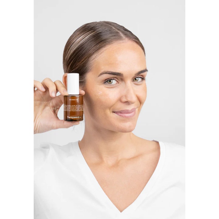 Niche Beauty Lab Transparent Lab Ascorbic C15 Serum 30 ml i brun glasflaske holdes af smilende kvinde