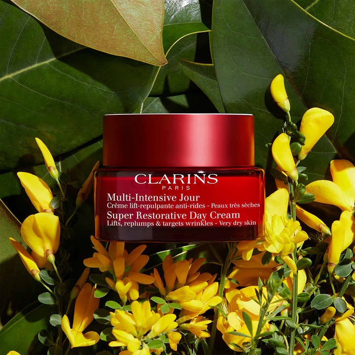 Clarins Super Restorative Day Cream 50 ml opstrammende dagcreme i rød krukke omgivet af grønne blade og gule blomster.