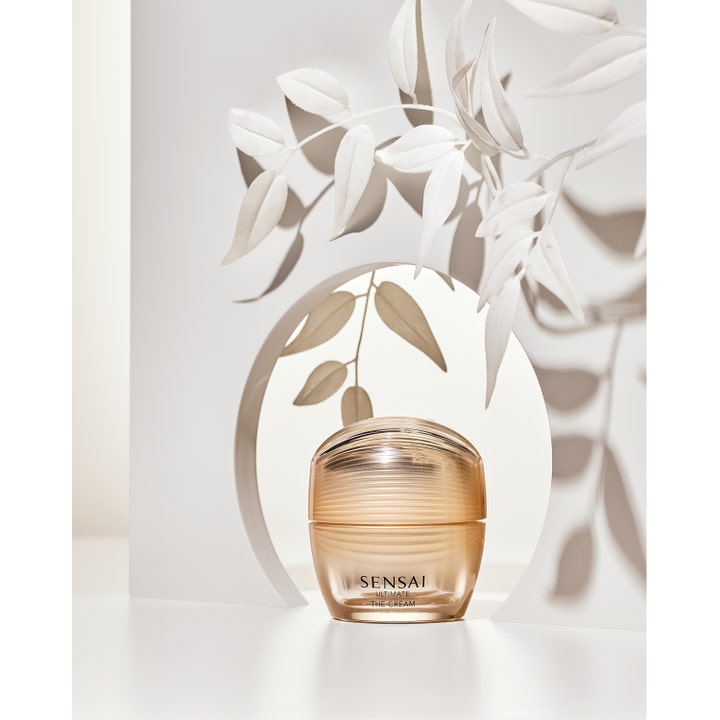 Sensai Ultimate The Cream 40 ml ansigtscreme i en luksuriøs guldkrukke omgivet af hvide blade og bløde skygger.
