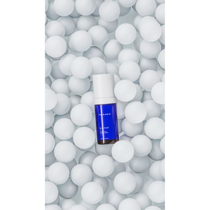 Niche Beauty Lab Theramid Hapca Filler 30 ml fugtgivende serum i blå flaske omgivet af hvide kugler.