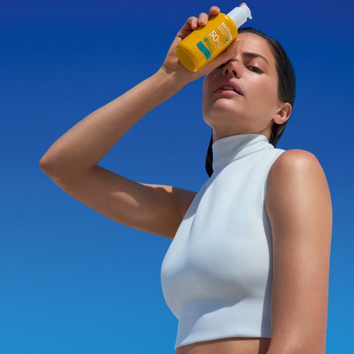 Biotherm Waterlover Sun Milk 200 ml solcreme SPF 50 i gul flaske holdt af en kvinde mod en klar blå himmel