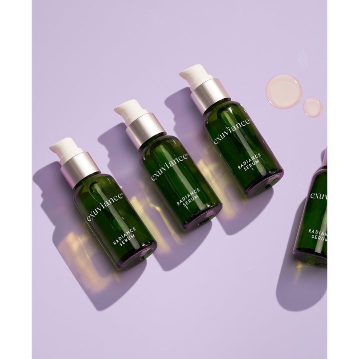 Exuviance Radiance Serum 30 ml glødgivende serum i grønne glasflasker med hvid pumpe og lyserøde dråber