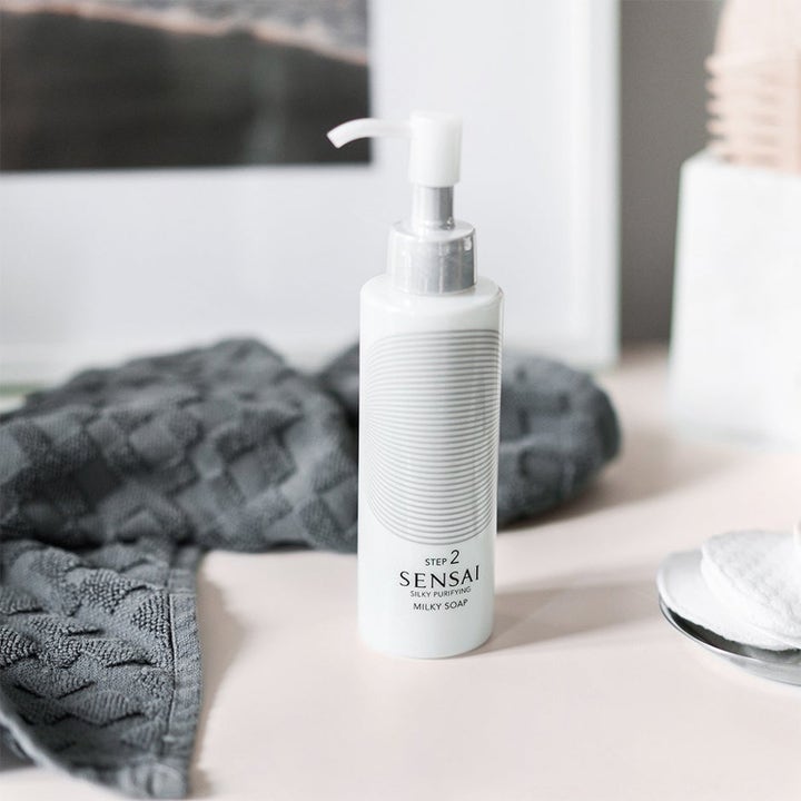 Sensai Silky Purifying Milky Soap 150 ml ansigtsrens i hvid flaske med pumpe ved siden af en grå klud