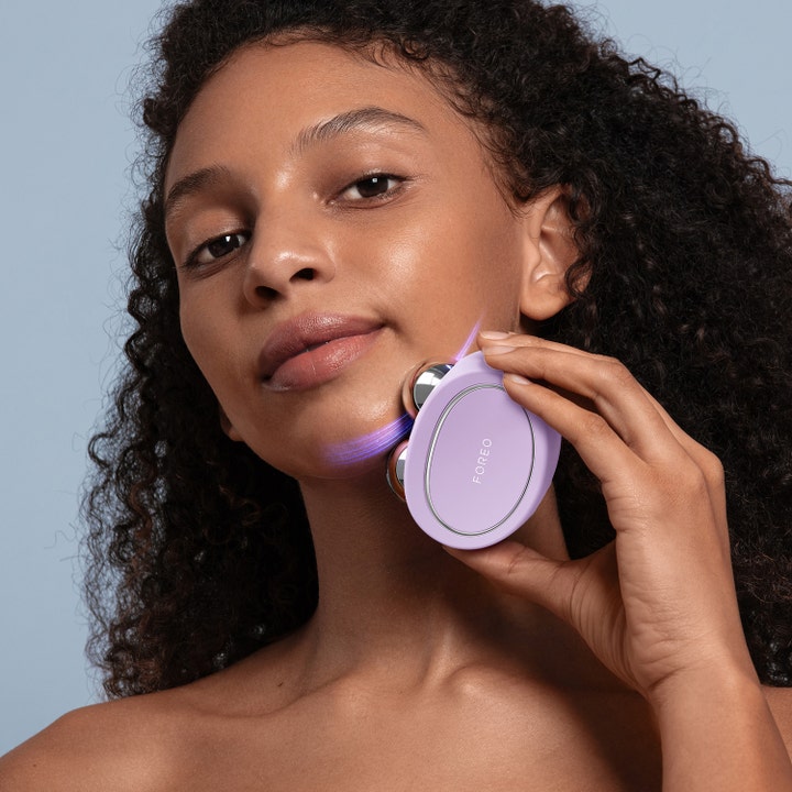 FOREO BEAR 2 Lavender 1 stk opstrammende mikrostrøm anvendt på kæbelinjen af en kvinde med lilla lys.