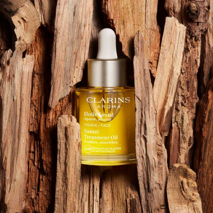 Clarins Santal Treatment Oil 30 ml beroligende ansigtsolie i glasflaske omgivet af rustikke træstykker