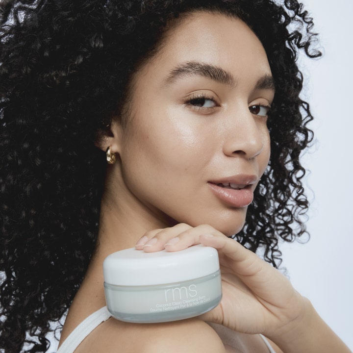 RMS Beauty Coconut Clean Cleansing Balm 100 g blødgørende ansigtsrens i hvid krukke holdt af model med sund glød