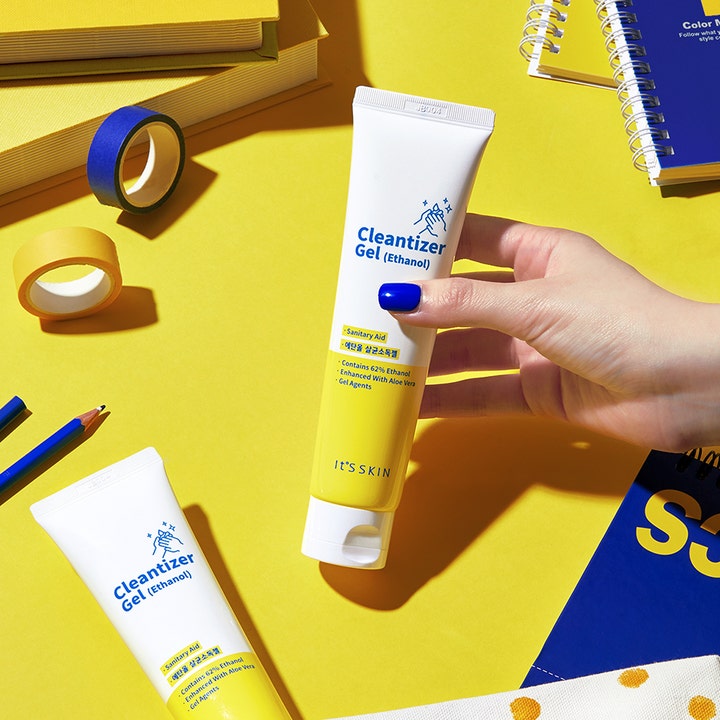 It'S SKIN Cleantizer Gel 100 ml beroligende håndsprit i hvid og gul tube holdt af en hånd mod gul baggrund