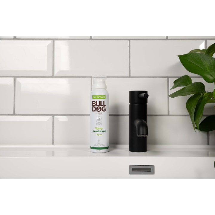 Bulldog Spray Deodorant Original 125 ml herredeodorant i hvid sprayflaske ved siden af sort armatur og plante.