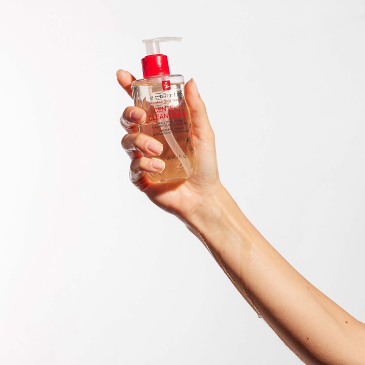 Erborian Centella Cleansing Oil 180 ml beroligende ansigtsrens i en klar flaske med rød pumpe holdt af en hånd